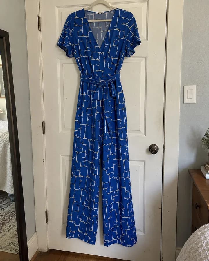 Hanger shot: a blue printed wrap jumpsuit hanging on a door